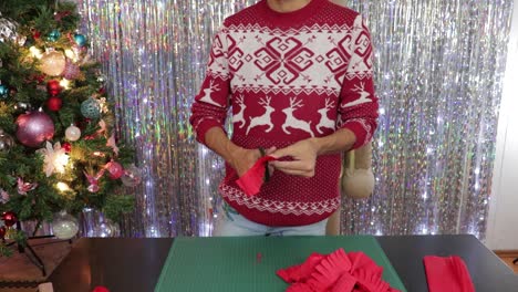 man in christmas jumper cutting red crepe paper to craft decorations