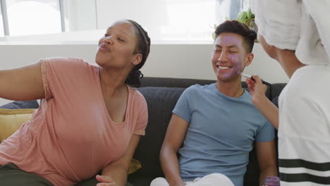 Young-biracial-woman-applies-makeup-to-a-young-Asian-man-at-home