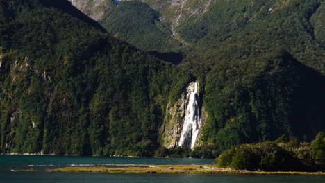 zoom in lady bowen falls while cruising past snow capped mountains at milford sound