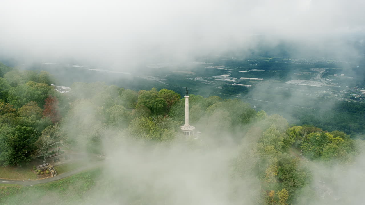 The Point Park statue emerges through thick mountain fog in a wide drone shot revealing the sweeping valley below