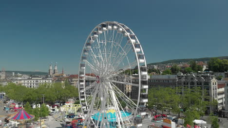 Beautiful-orbiting-aerial-drone-shot-rising-up-and-around-amusement-park-Ferris-wheel-with-the-city-of-Zürich,-Switzerland-in-the-background-during-Zürichfest