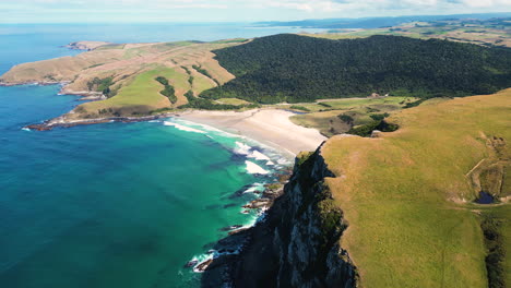 drone fly above scenic cliff coastline revealing lonely pristine beach in pūrākaunui small settlement in otago, in the south island of new zealand aerial footage