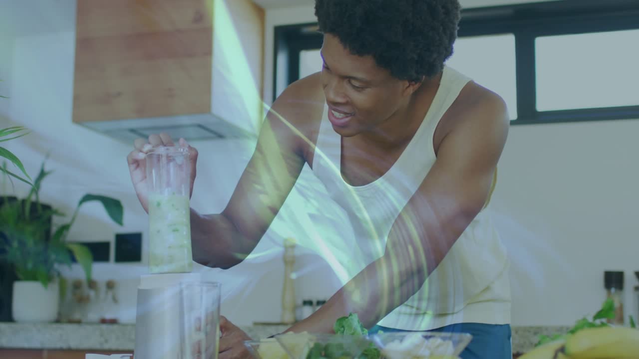Man preparing healthy smoothie in kitchen adding fruit into blender mixing with lens flare on hands