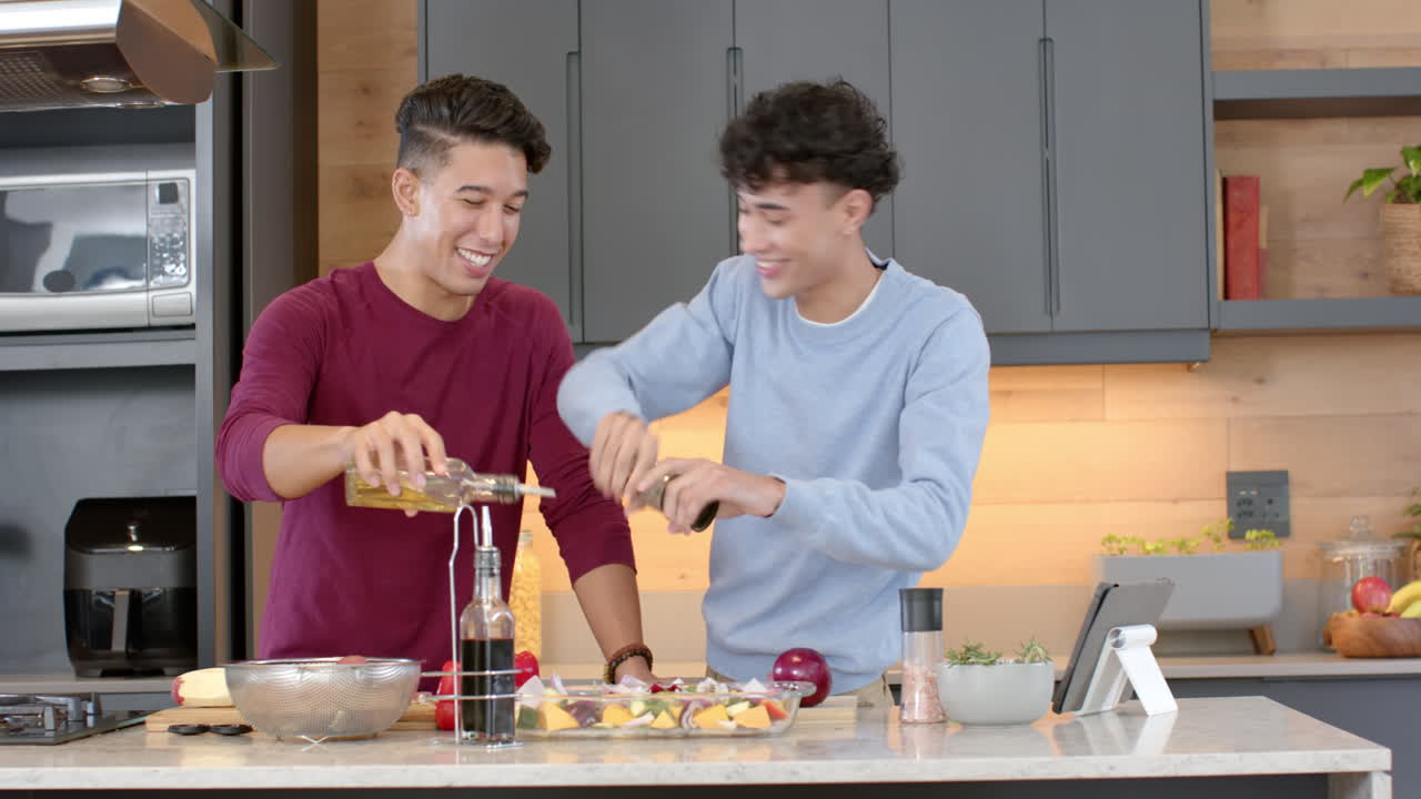 Cooking , multiracial gay couple preparing meal in modern kitchen, smiling and enjoying, at home