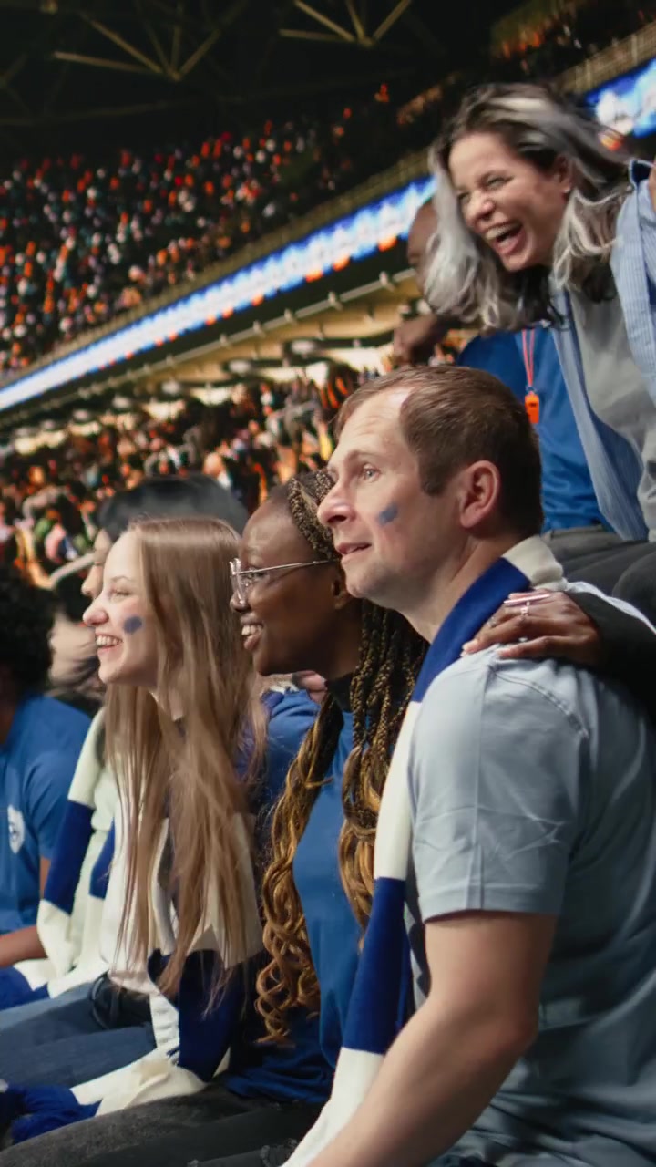 Video vertical: Líder de la hinchada de piel oscura entre la multitud de aficionados azules dirigiendo los cánticos del estadio.