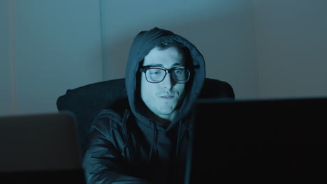 young man in hood working on laptop late at night