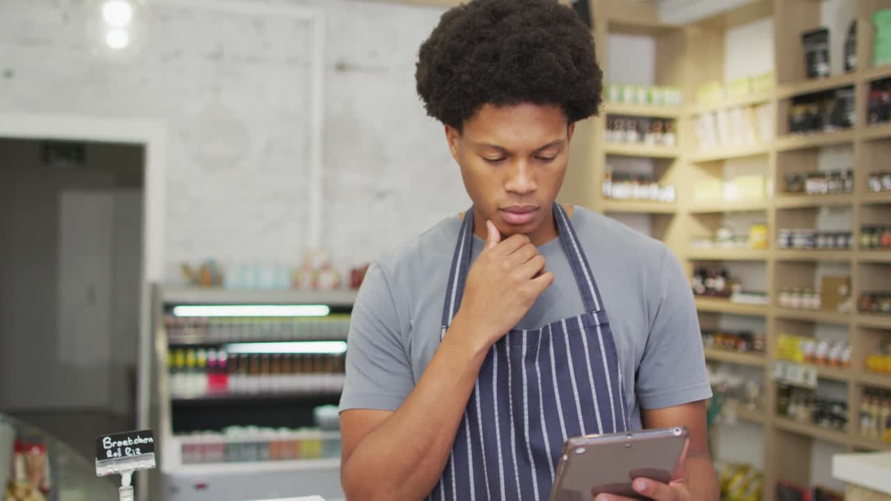 Animation of thoughtful biracial waiter using tablet in coffee shop