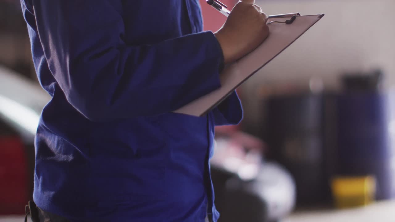 sección media de la mecánica femenina tomando notas en el clipboard en una estación de servicio de coches