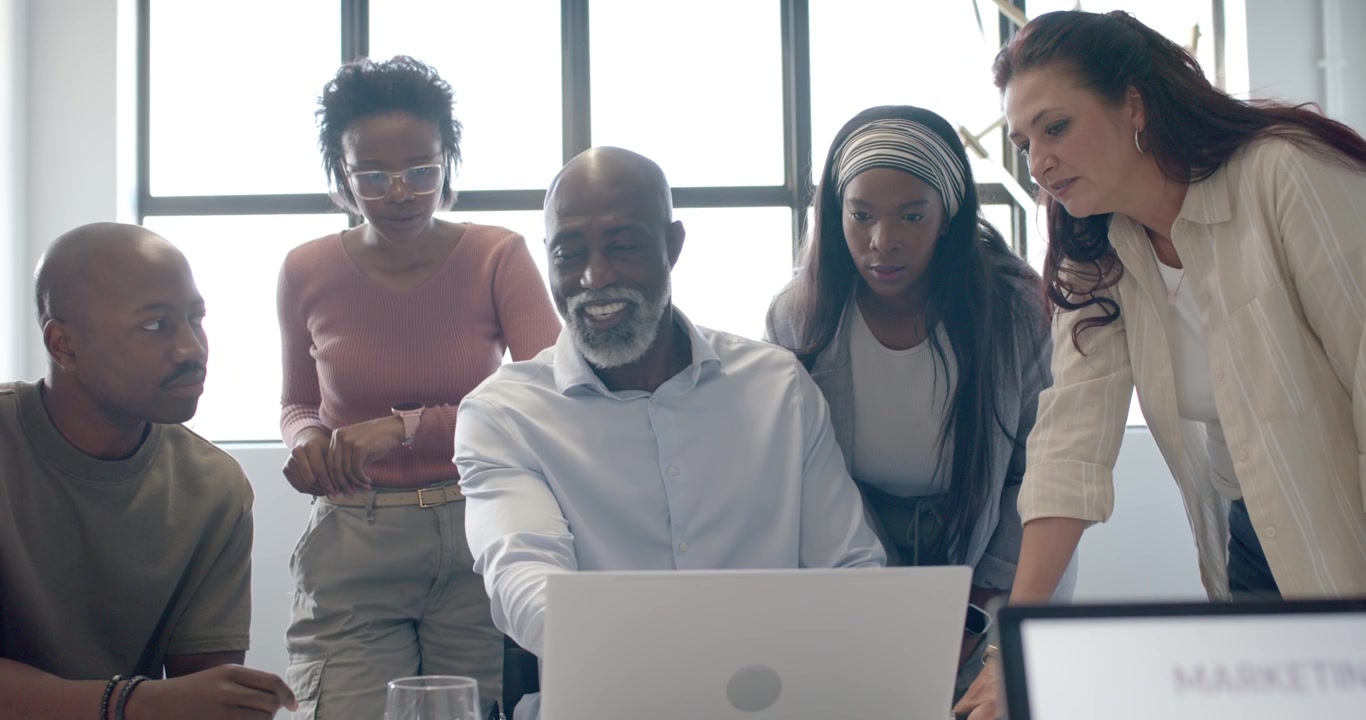 Diverse coworkers leaning around laptop and monitor, responding to marketing funnel, aligning plan