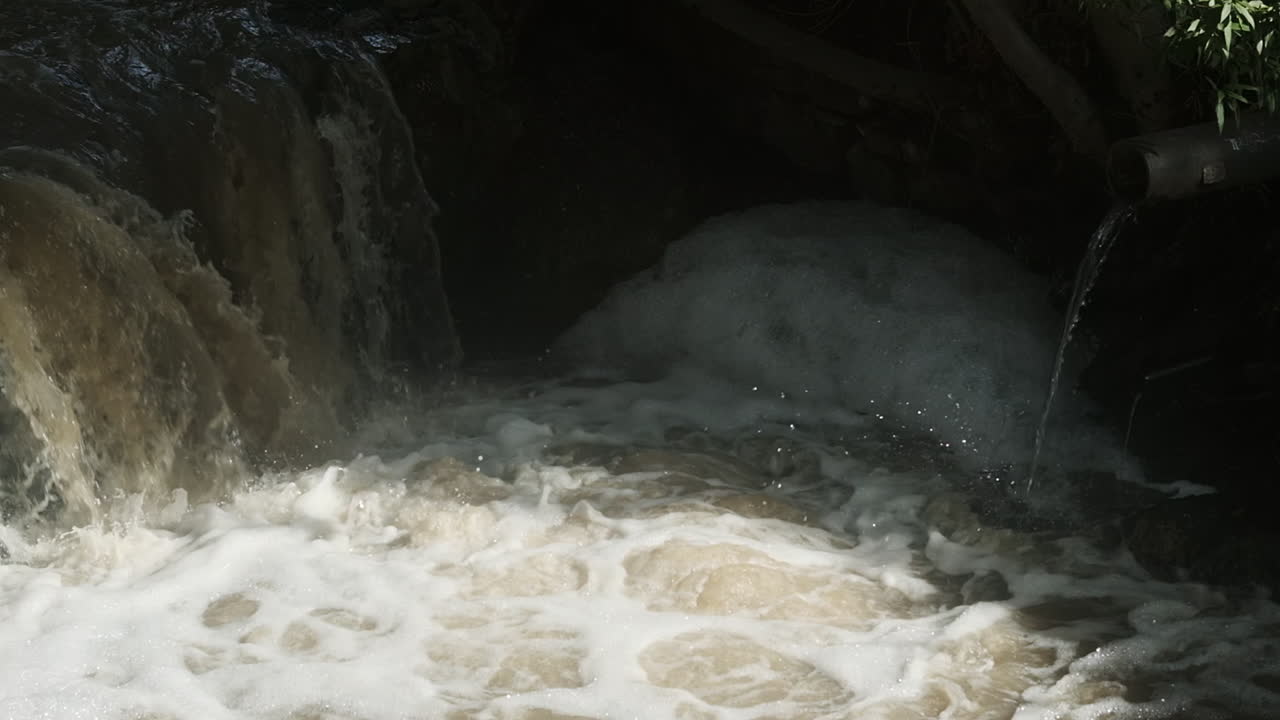 Water pours down a stream and drainage pipes creating foam