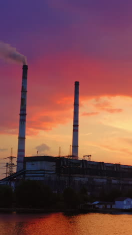industrial area at sunset. factory near the river on the beautiful pink sky. harmful manufacture with smoke goes from industrial pipe in the evening. vertical video