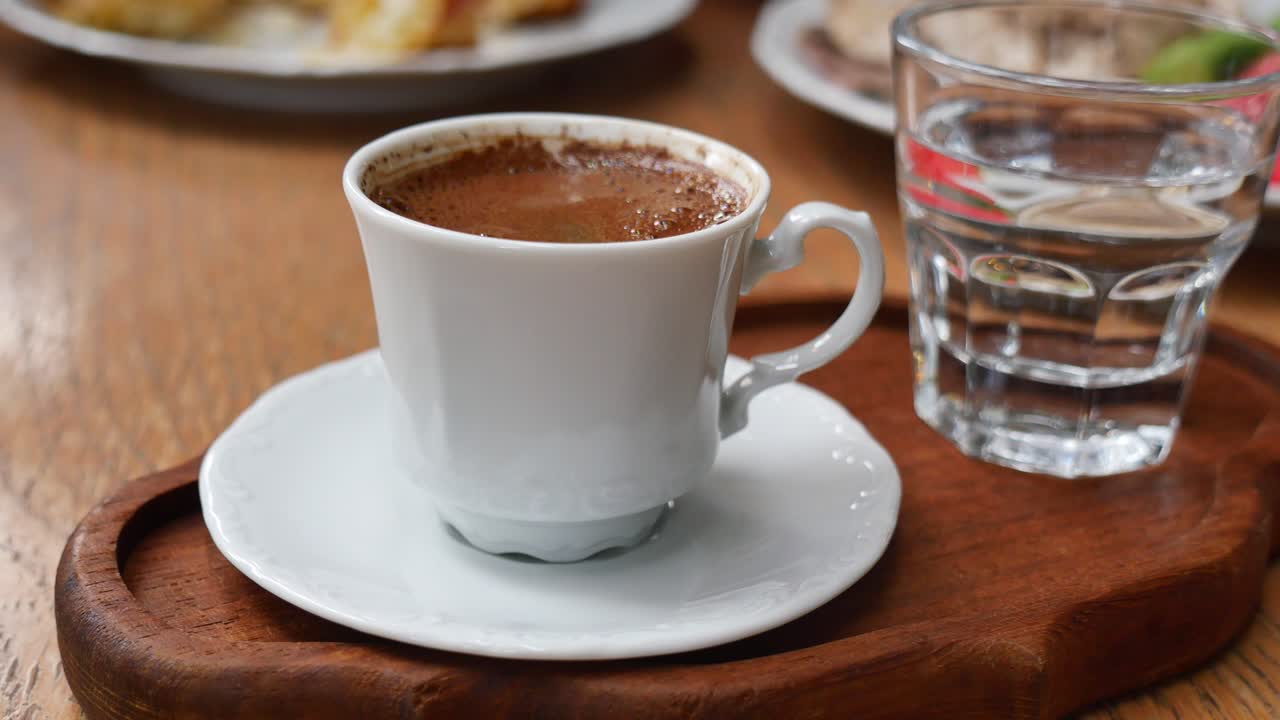 A cup of Turkish coffee and a glass of water on a wooden tray