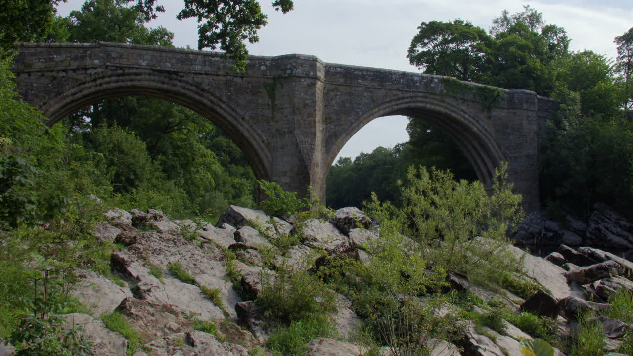 Wide shot looking up to devils bridge from the river Lune with rocks in foreground