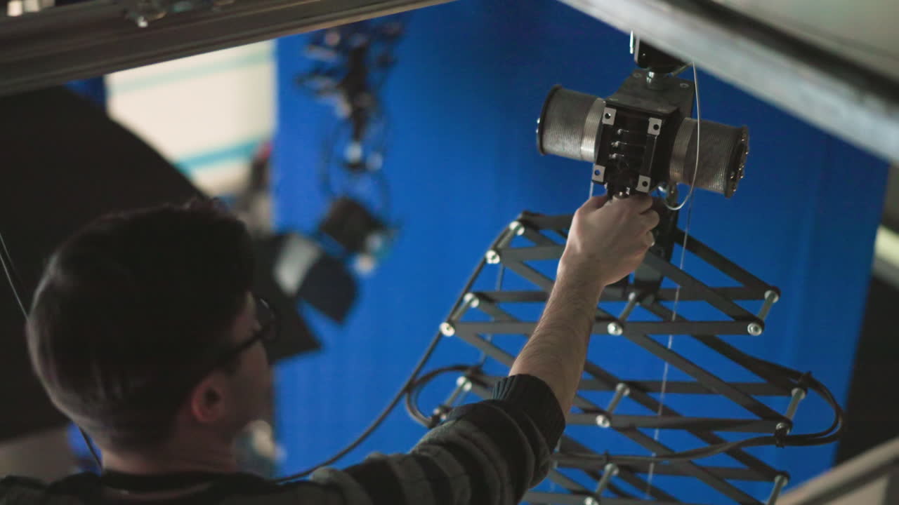 Technician adjusting overhead lighting equipment, positioning light fixture carefully in a studio environment, preparing lighting rig for precise production use, focusing on alignment and setup