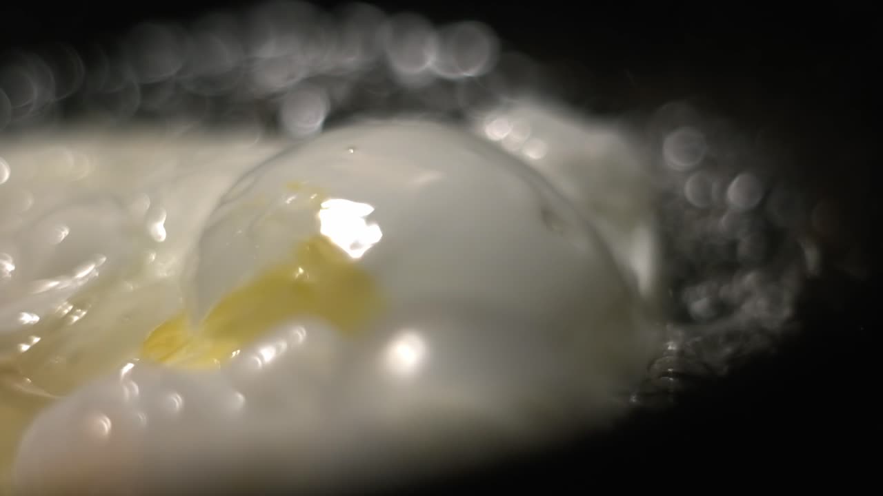 Egg white bubble close up in a black frying pan with hot boiling oil with soft bokeh