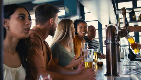 multi-cultural group of friends in sports bar celebrating as they watch game on tv