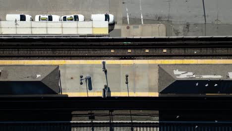 Una-Vista-De-Arriba-Hacia-Abajo-Directamente-Sobre-Una-Estación-De-Tren-Mientras-Las-Palomas-Vuelan-Debajo-Del-Dron-En-Un-Día-Soleado