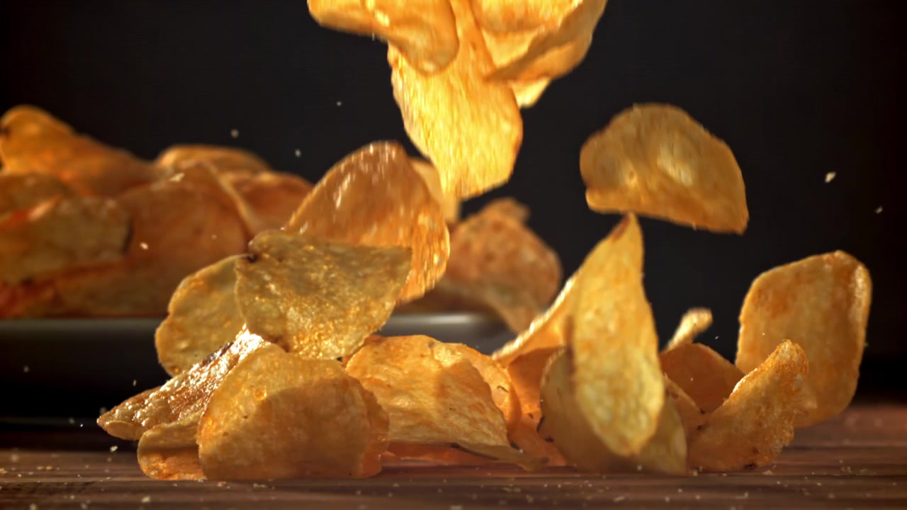 Crispy Potato Chips Falling onto a Wooden Table in Slow Motion