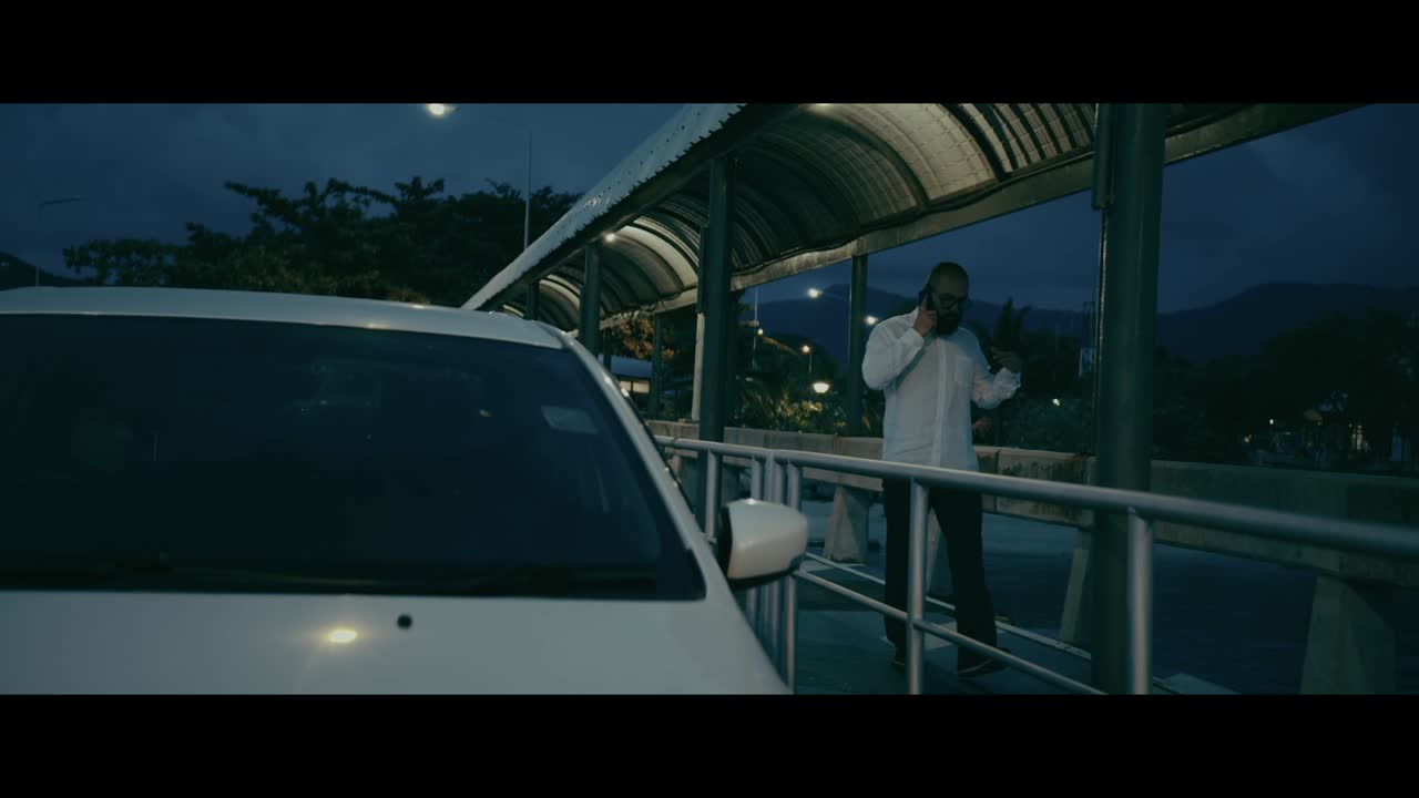 Man talking on phone near a parked car at night