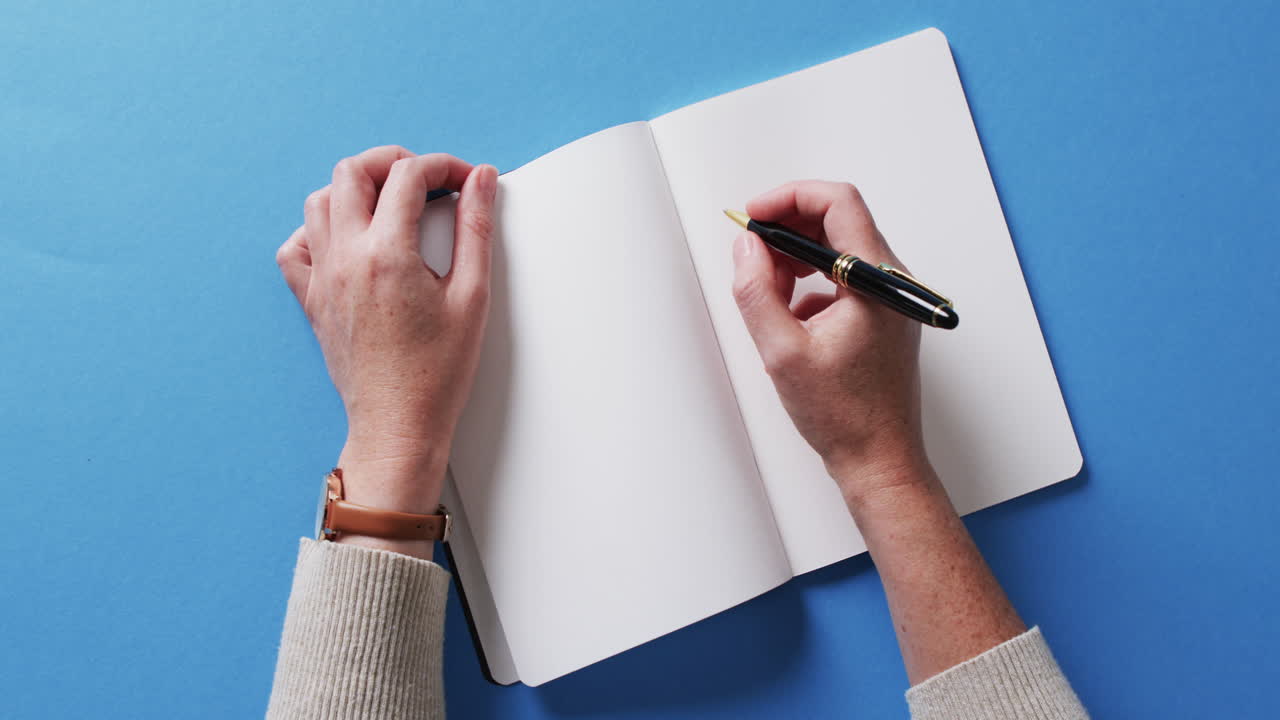 Close up of hand writing with pen on book with copy space on blue background in slow motion