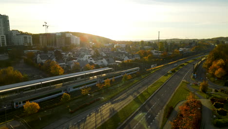 passenger railway train arriving at gdynia redlowo station early in the morning at bright autumn sunrise aerial view, several cars moving on droga gdynska highway