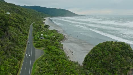 Scenic-aerial-view-of-wild,-rugged-and-remote-West-Coast-with-waves-rolling-into-beach-shoreline-on-the-South-Island-of-New-Zealand-Aotearoa