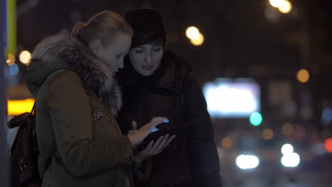 women friends using tablet pc when waiting for bus in the street