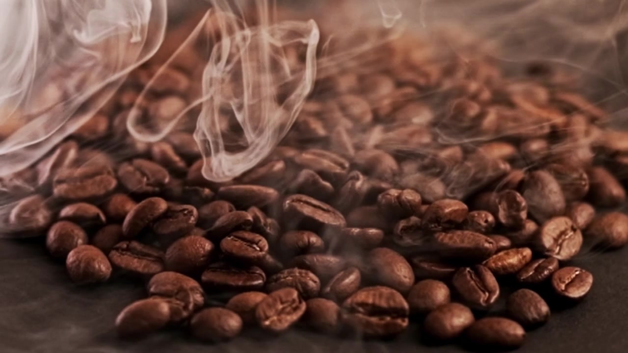 Chicchi di caffè tostati molto fumosi e vaporosi su una superficie nera