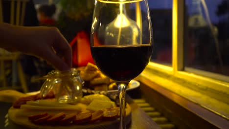 Male-hand-picking-cheese-and-sausage-off-platter-with-red-wine-glass-in-foreground-in-candle-lit-restaurant-setting