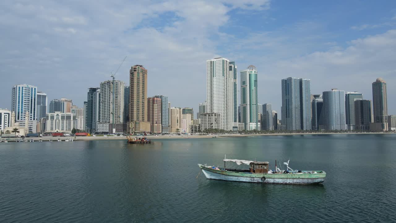 Drone view of the traditional Arabian fishing boats moored on the surface of Gulf Sea, Mordren skyscrapers in the background