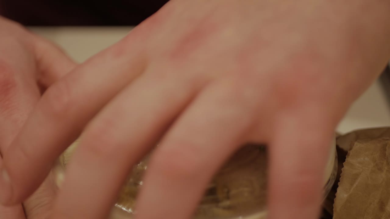 un hombre arrugando lentamente una bolsa de papel marrón para revelar una deliciosa cocina tailandesa, lista para comer - cerrar