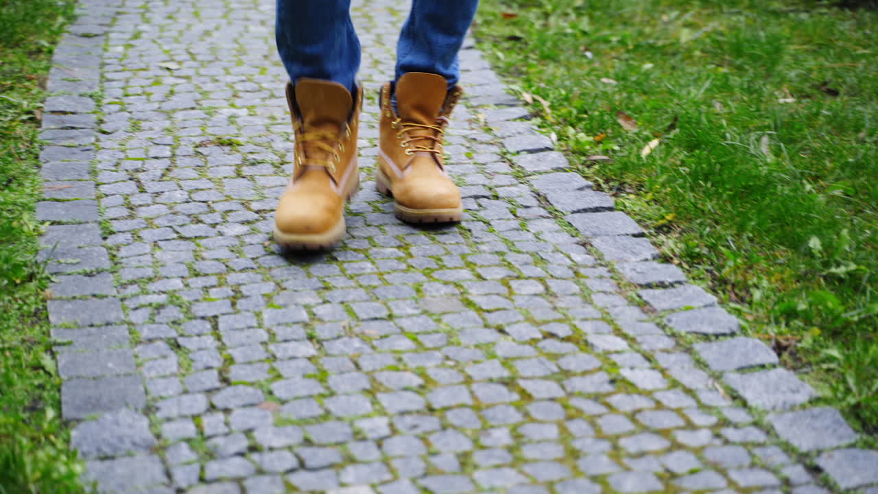 Stylish man's legs outdoors. Male in brown boots walking a stone path. Man's feet wearing jeans and shoes walks on terrace in autumn time. Close-up.
