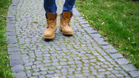 stylish man's legs outdoors. male in brown boots walking a stone path. man's feet wearing jeans and shoes walks on terrace in autumn time. close-up.