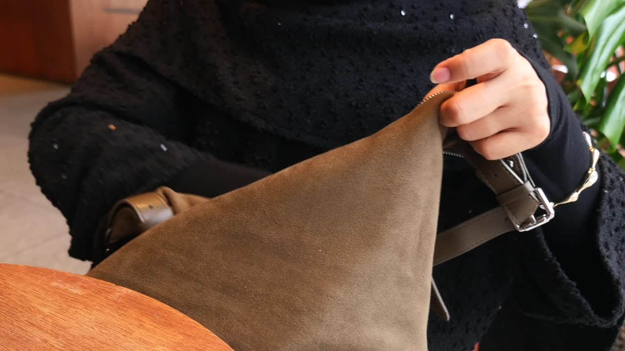 Close-up of a person opening a brown suede handbag