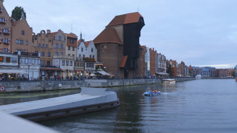 Toma-Panorámica-Desde-Un-Puente-En-El-Río-Martwa-Gdansk-Polonia-Europa,-Vista-Del-Barco-Grúa-Zuraw-Con-Turistas-Y-Edificios-De-Arquitectura-Tradicional