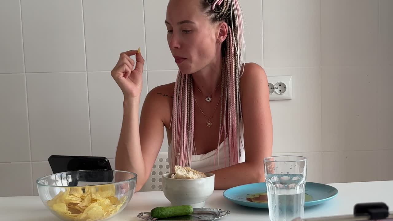 Junge Frau mit Zöpfen isst Chips an einem Tisch