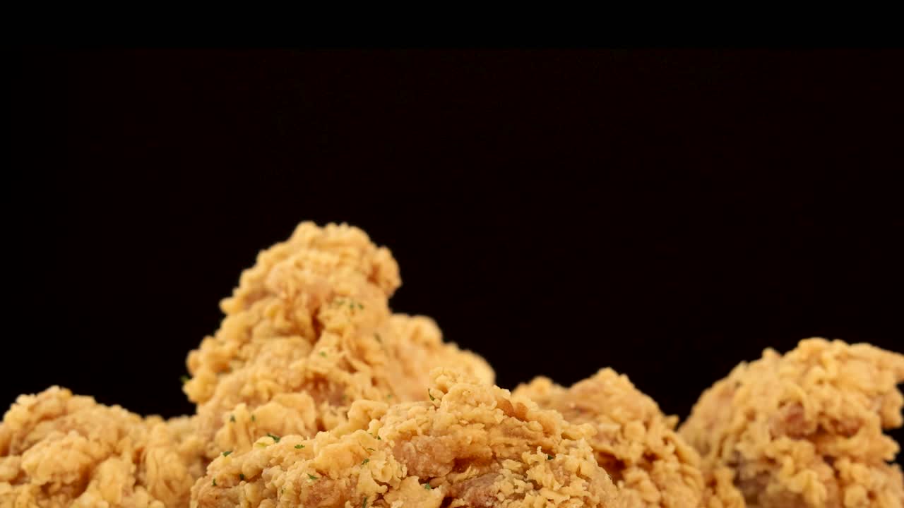 Golden, crispy fried chicken breasts and thighs rotate slowly against a dark background, highlighting crunchy texture and seasoning in dramatic studio lighting