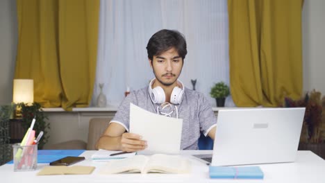 Estudiante-Varón-Trabajando-Entre-Papel-Y-Computadora-Portátil.