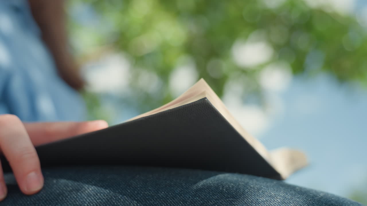 여성이 페이지를 넘기는 모습, 여름 바람이 부는 배경 속에서 노트북 페이지를 넘기는 여성, 생동감 넘치는 초록색 보케 배경을 뒤로 하고 섬세하게 저널 페이지를 넘기는 백인 여성