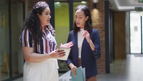 two focused biracial businesswomen working together, using tablet in modern office