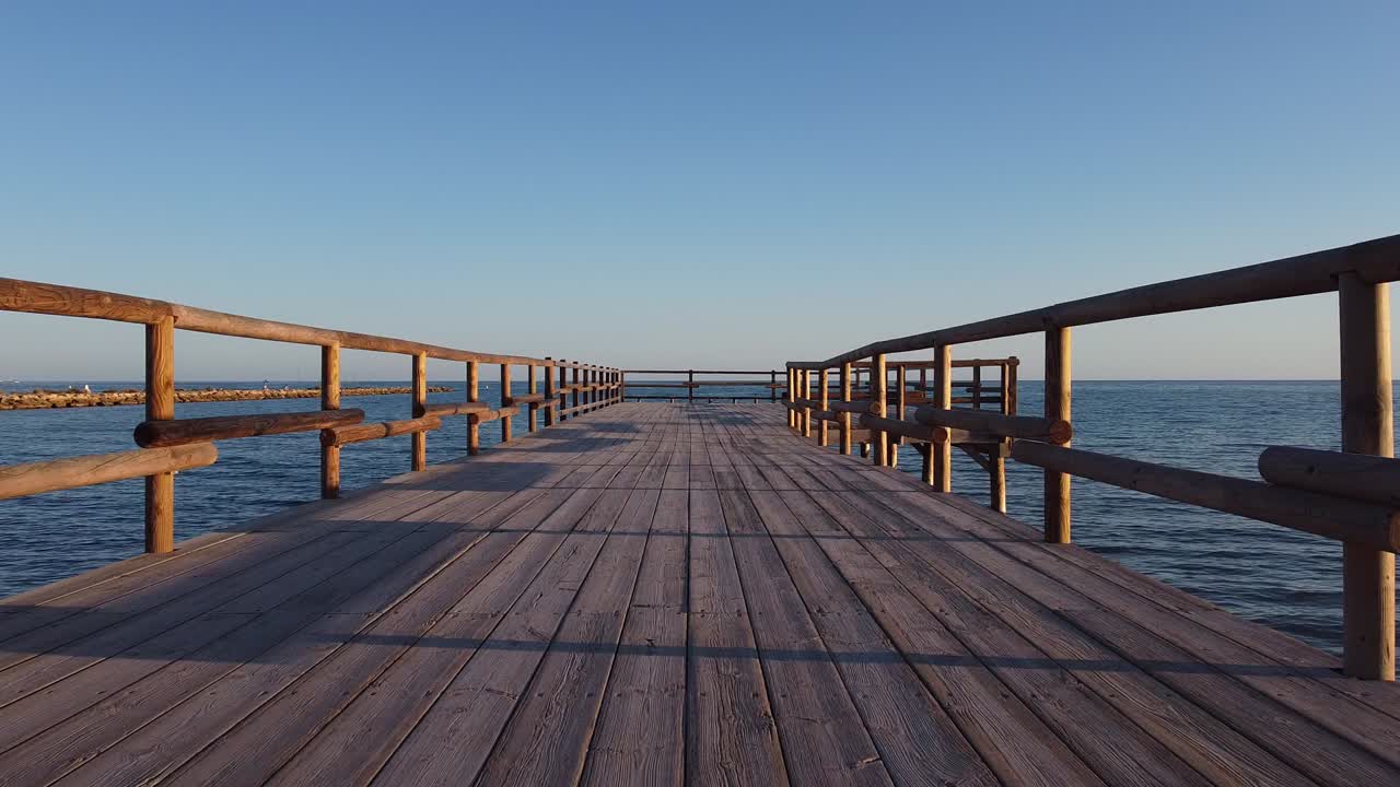 A fishing pier stretching out over the ocean - flying low just over the pier and then over the railing and the open sea