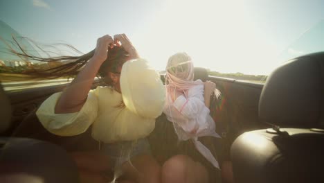 two young women enjoying a sunny convertible ride with hair blowing in the wind