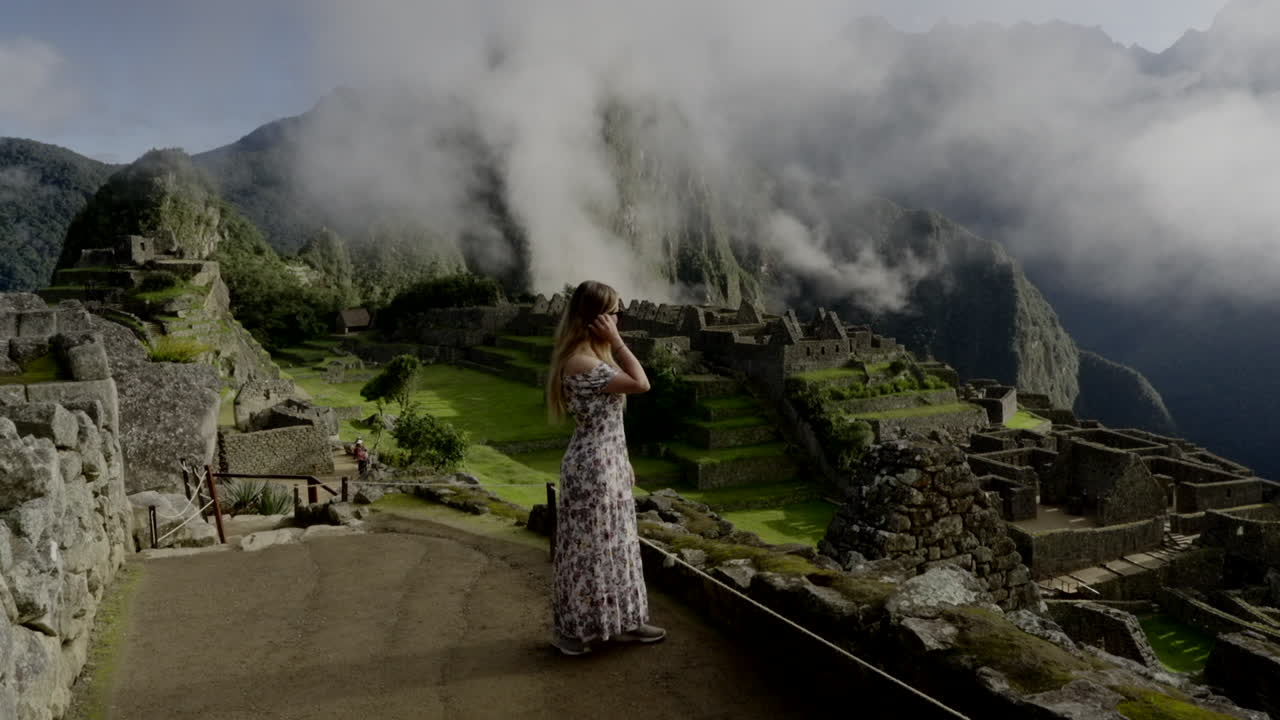 Tourist woman in dress inside Machu Picchu lost city watches landscape. Wanderer solo travel in Peru