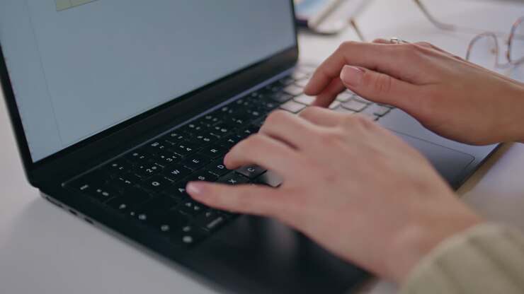 Nahaufnahme einer Frau, die an einem Laptop an ihrem Arbeitsplatz tippt.