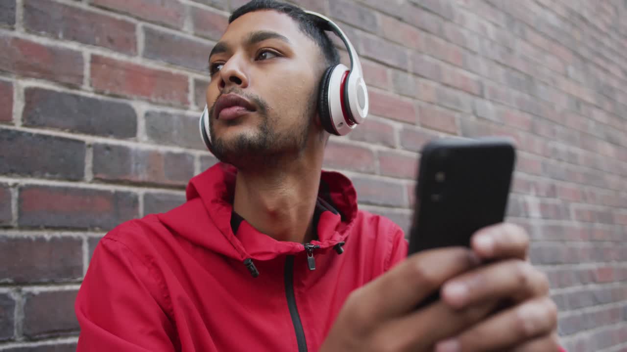 hombre de raza mixta con auriculares, usando un teléfono inteligente en la calle
