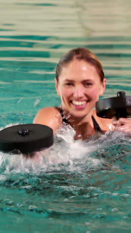 vertical video of fit woman doing aqua aerobics in the pool with foam dumbbells in the leisure cente