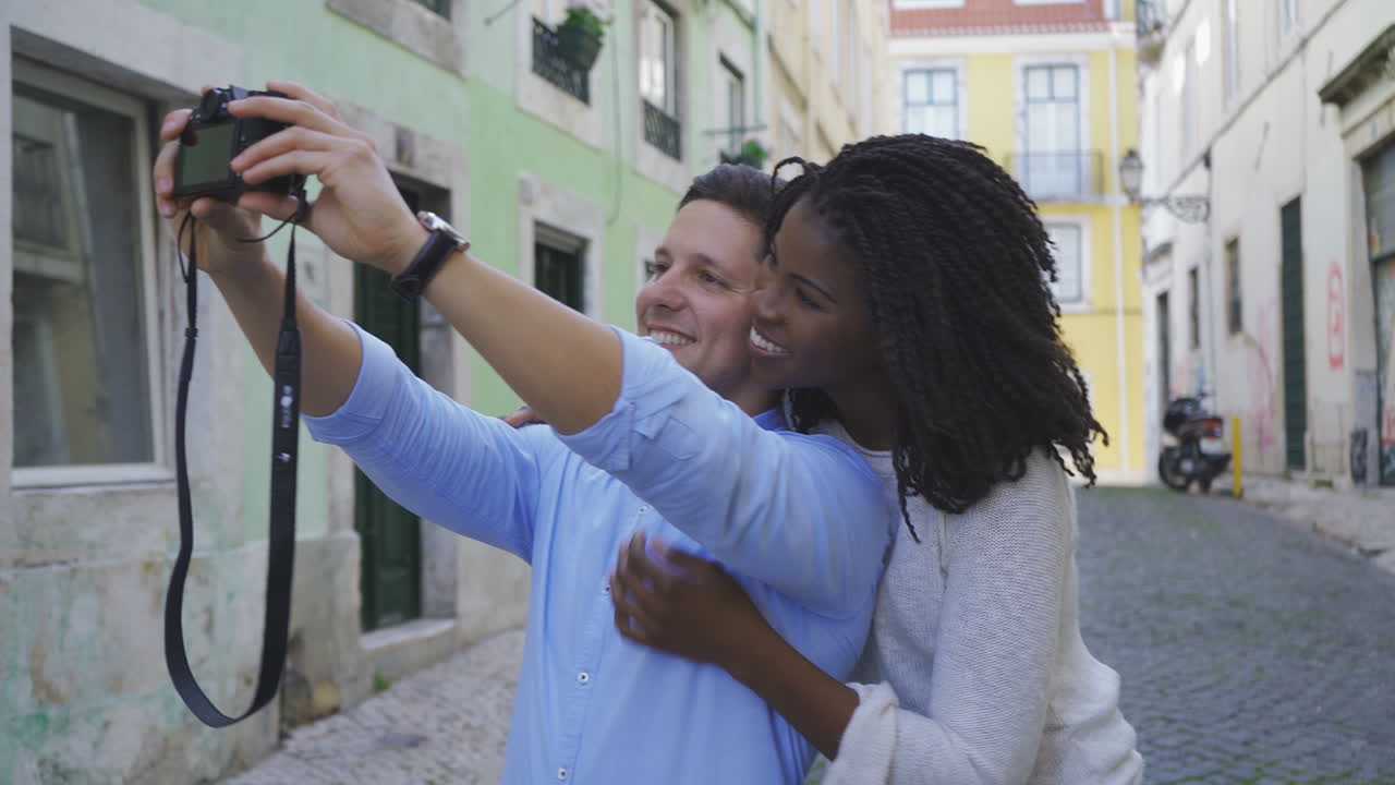 una pareja multirracial sonriente tomando una selfie con una cámara fotográfica.
