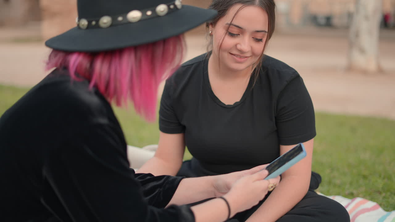 Two young women sitting in a park and looking at a mobile phone