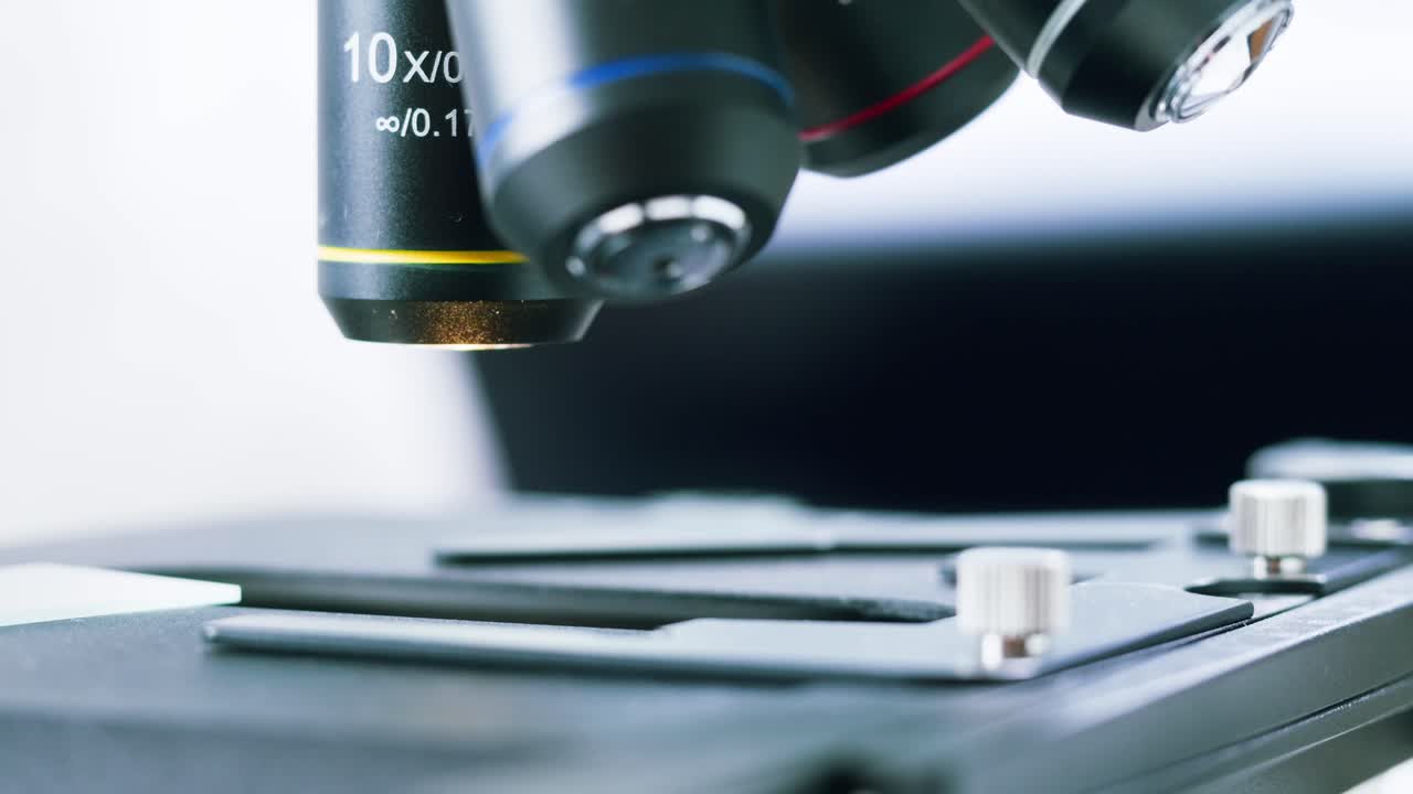 Gloved Hand Places Sample Slide on Microscope Stage