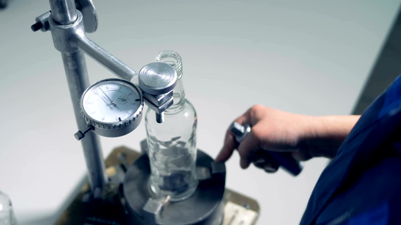 un trabajador de la fábrica está comprobando los parámetros de tamaño de una botella de vidrio